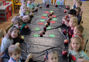 Przedszkolaki siedzą przy stole z całymi jabłkami